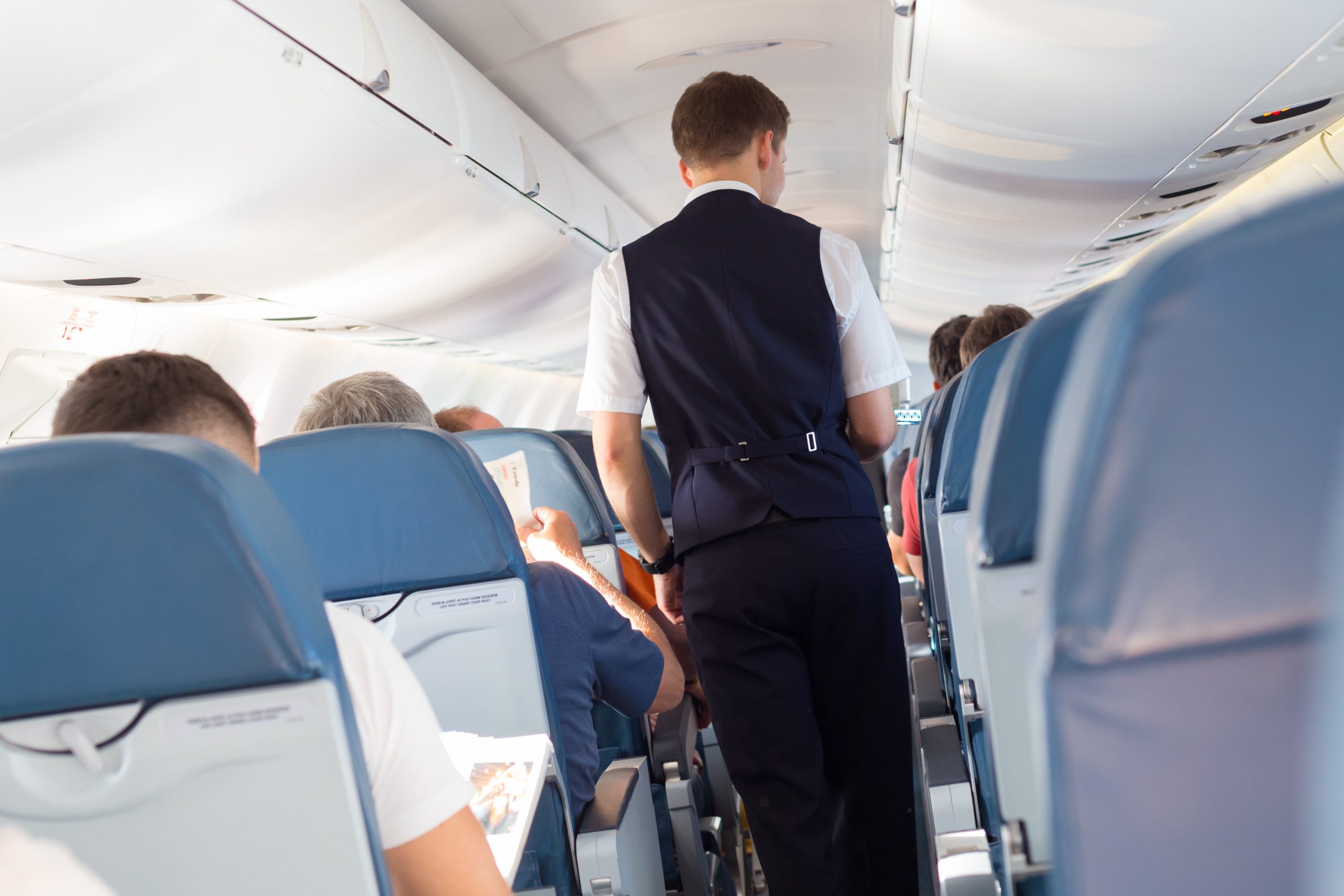 Interior of airplane with passengers on seats and steward walking the aisle.